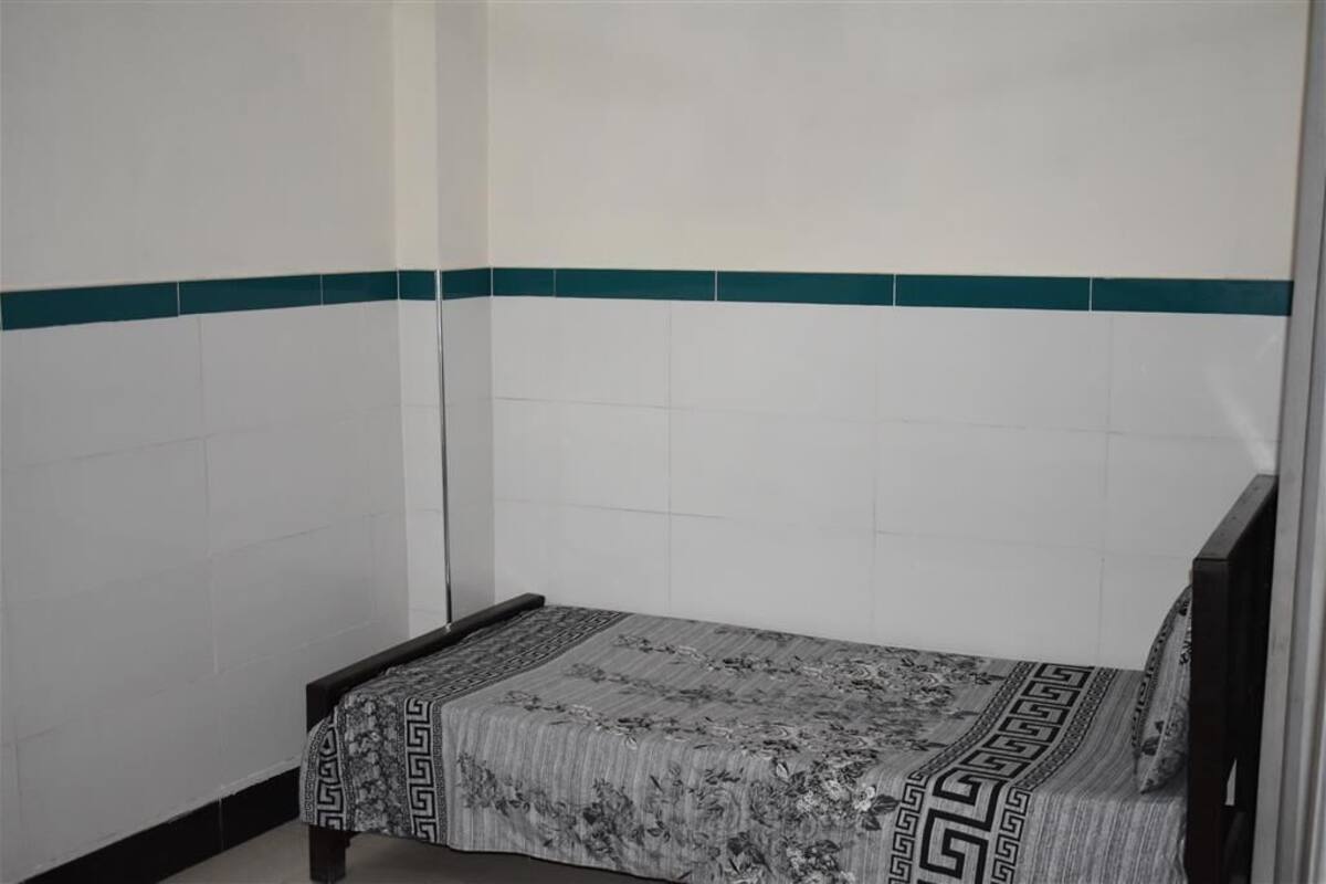 Una habitación pequeña con cama individual, colcha estampada y una franja verde en la pared.