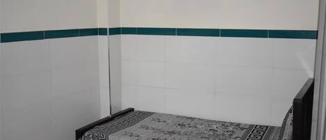 Una habitación pequeña con cama individual, colcha estampada y una franja verde en la pared.