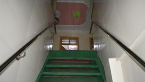 Eine Treppe mit grünen Teppichstufen, weißen Fliesenwänden und einer Holztür am oberen Ende.