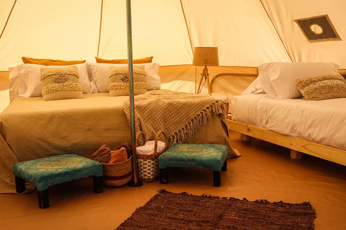 A tented accommodation with two beds, a small table, and a bench.