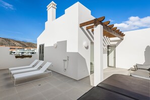 Une terrasse moderne avec des murs blancs, une pergola et un espace piscine équipé de chaises longues.