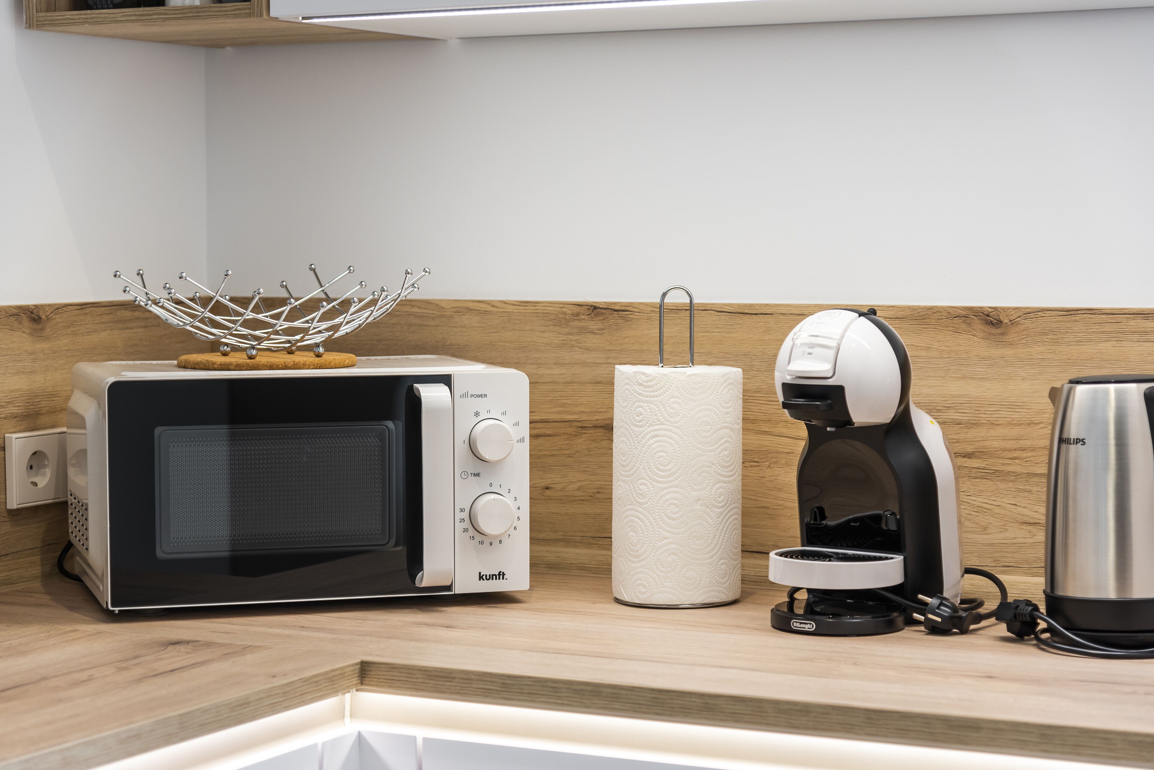 Eine Küche mit Mikrowelle, Kaffeemaschine und Papierhandtuchhalter auf einer Holzausziehtischplatte.