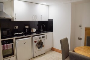 A compact kitchen with a microwave, toaster, and washing machine, a small dining area with a table and chair, and white cabinetry. - Osborne Apartments (Eastbourne)