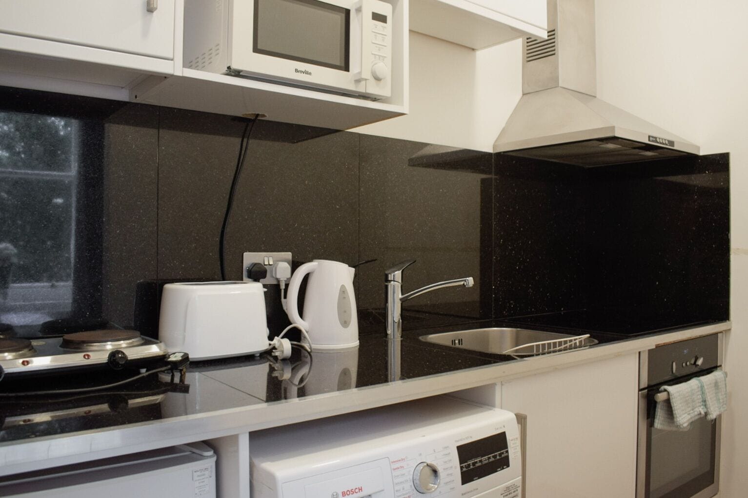 A modern kitchen with a microwave, toaster, kettle, sink, and Bosch dishwasher.