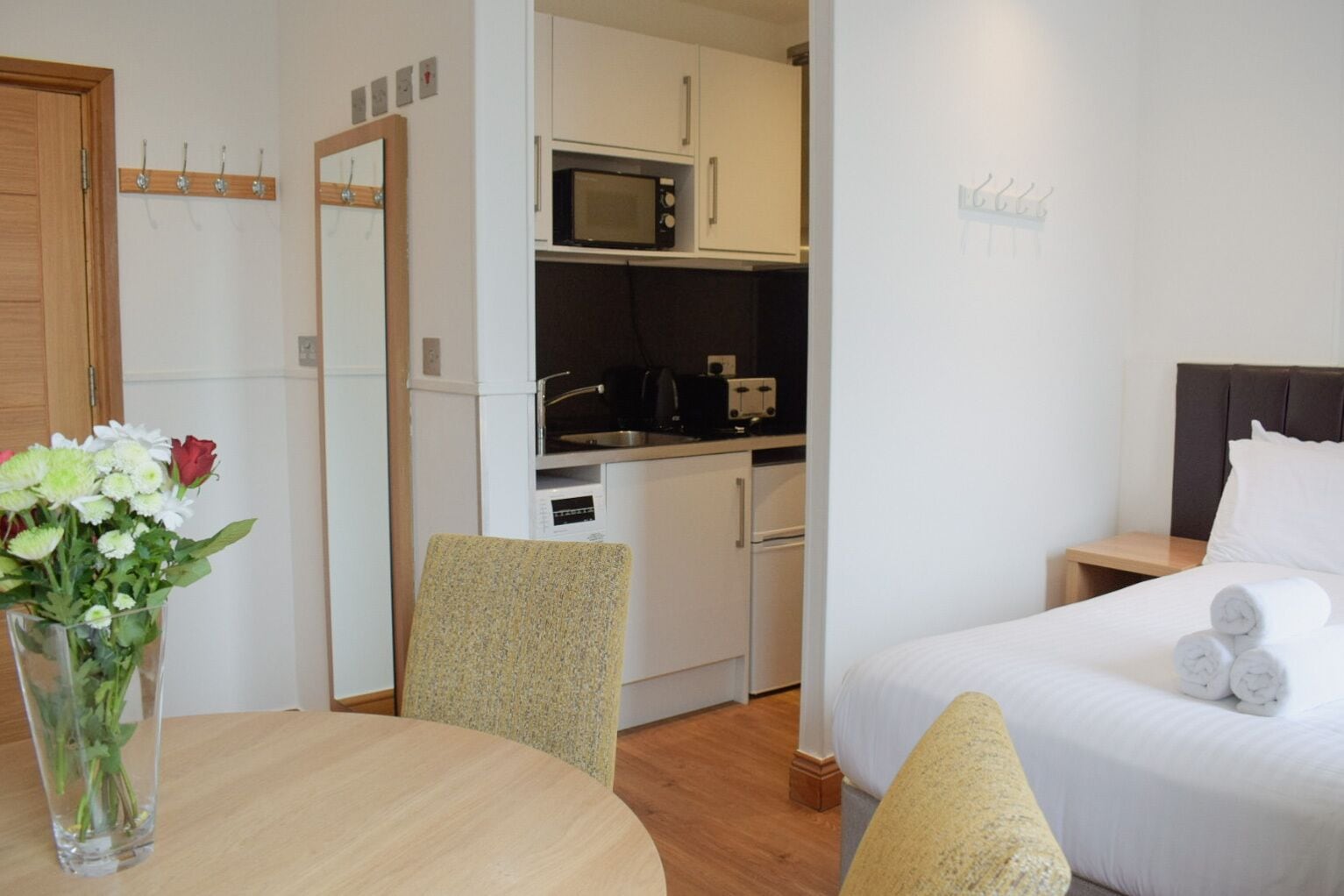 A compact hotel room with a bed, a small kitchenette, a dining area with a table and chairs, and a bathroom.
