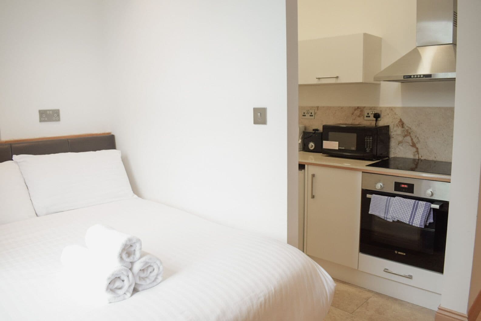 A hotel room with a bed, a kitchenette with a microwave, oven, and a small cabinet.