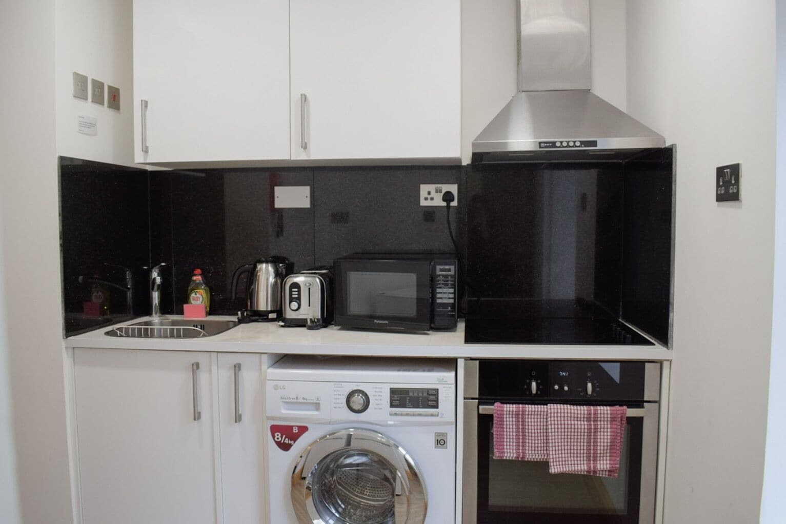 A compact kitchenette with a microwave, toaster, kettle, and a washing machine.