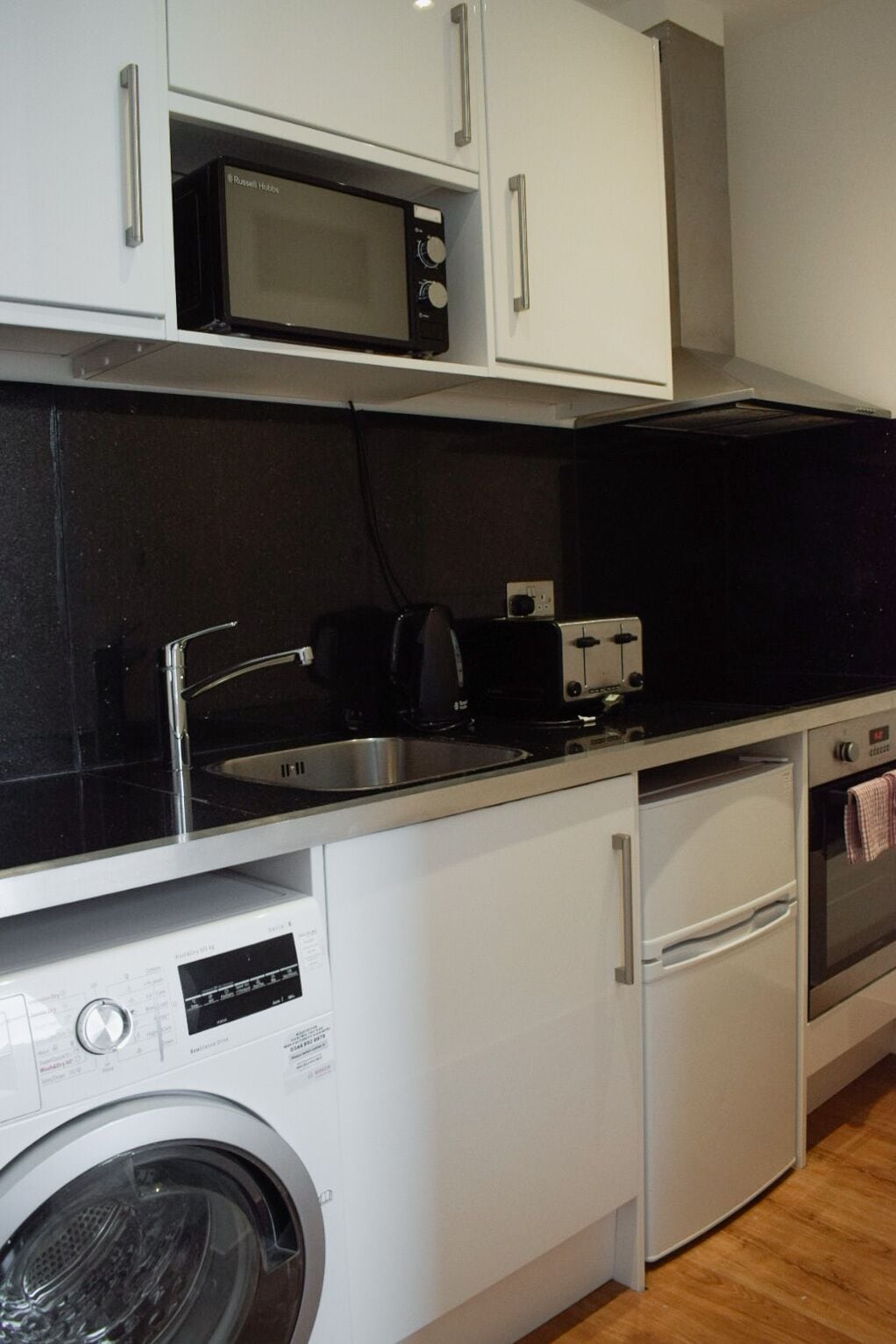 A compact kitchen with a washing machine, a microwave, a toaster, and a dishwasher.