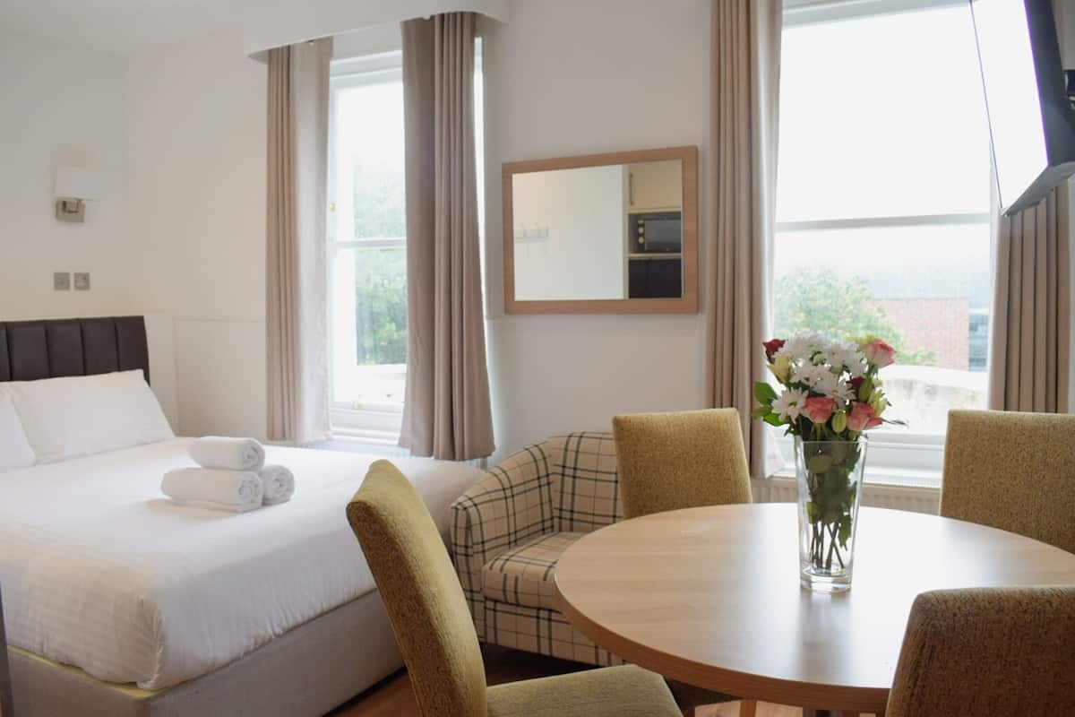 A hotel room with a bed, a round table with chairs, a vase of flowers, and a large window with curtains.