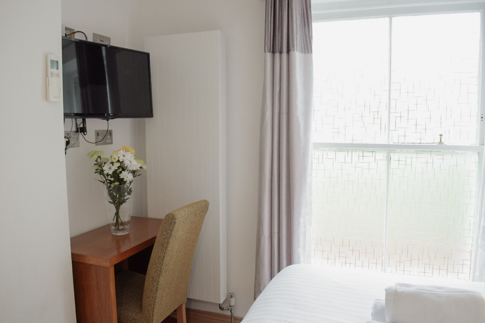 Ein Hotelzimmer mit Bett, Schreibtisch mit Stuhl, Fernseher und einem Fenster mit Vorhängen.
