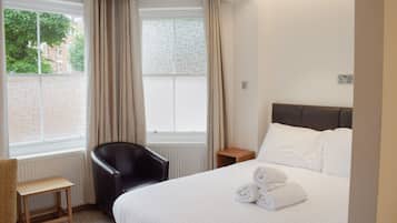 A hotel room with a bed, a chair, a small table, and a window with curtains.