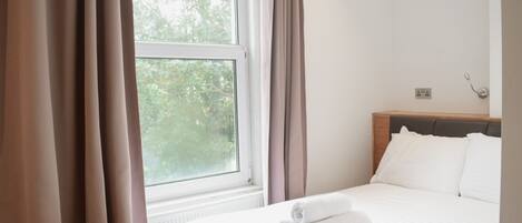 Una habitación de hotel con cama, ventana con cortinas y vista a árboles.