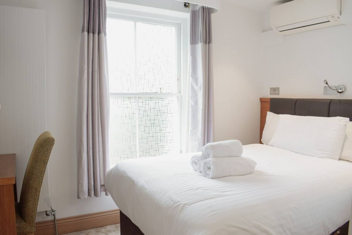A hotel room with a bed, a desk, a chair, and a window with curtains.