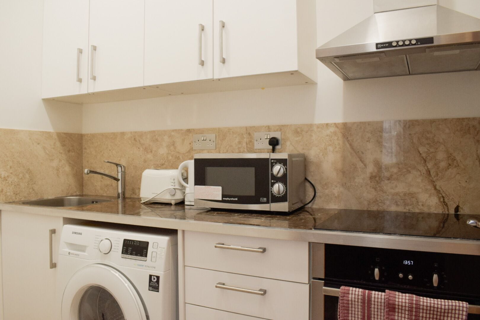 A compact kitchen with a washing machine, microwave, and oven.