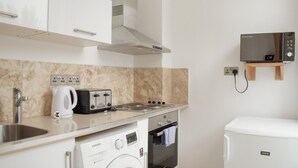 A compact kitchen with a washing machine, a microwave, and a toaster. - Osborne Apartments (Eastbourne)
