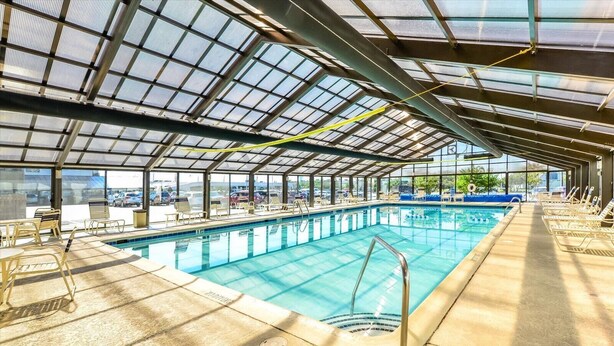 Una piscina interior con techo de cristal, sillas de descanso y vistas al aparcamiento exterior.