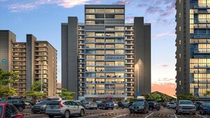 Un hotel de varios pisos con diseño moderno, que cuenta con balcones en cada nivel, un estacionamiento con varios autos y un cielo despejado con nubes.