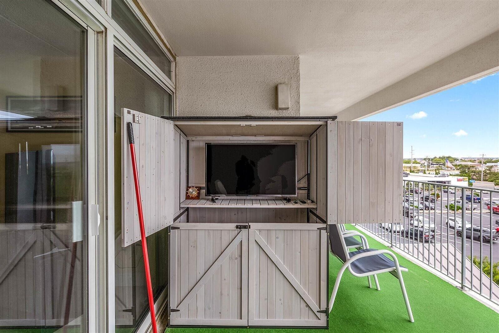 A balcony with a built-in TV, a wooden door, and a view of a parking lot.