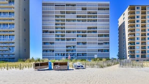 Un edificio de gran altura con varios balcones, ubicado en una playa de arena con una cerca de madera al frente.