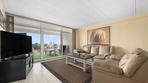 Una sala de estar moderna con un televisor de pantalla plana, un sofá color beige, una mesa de centro y un gran ventanal que ofrece vistas al exterior.