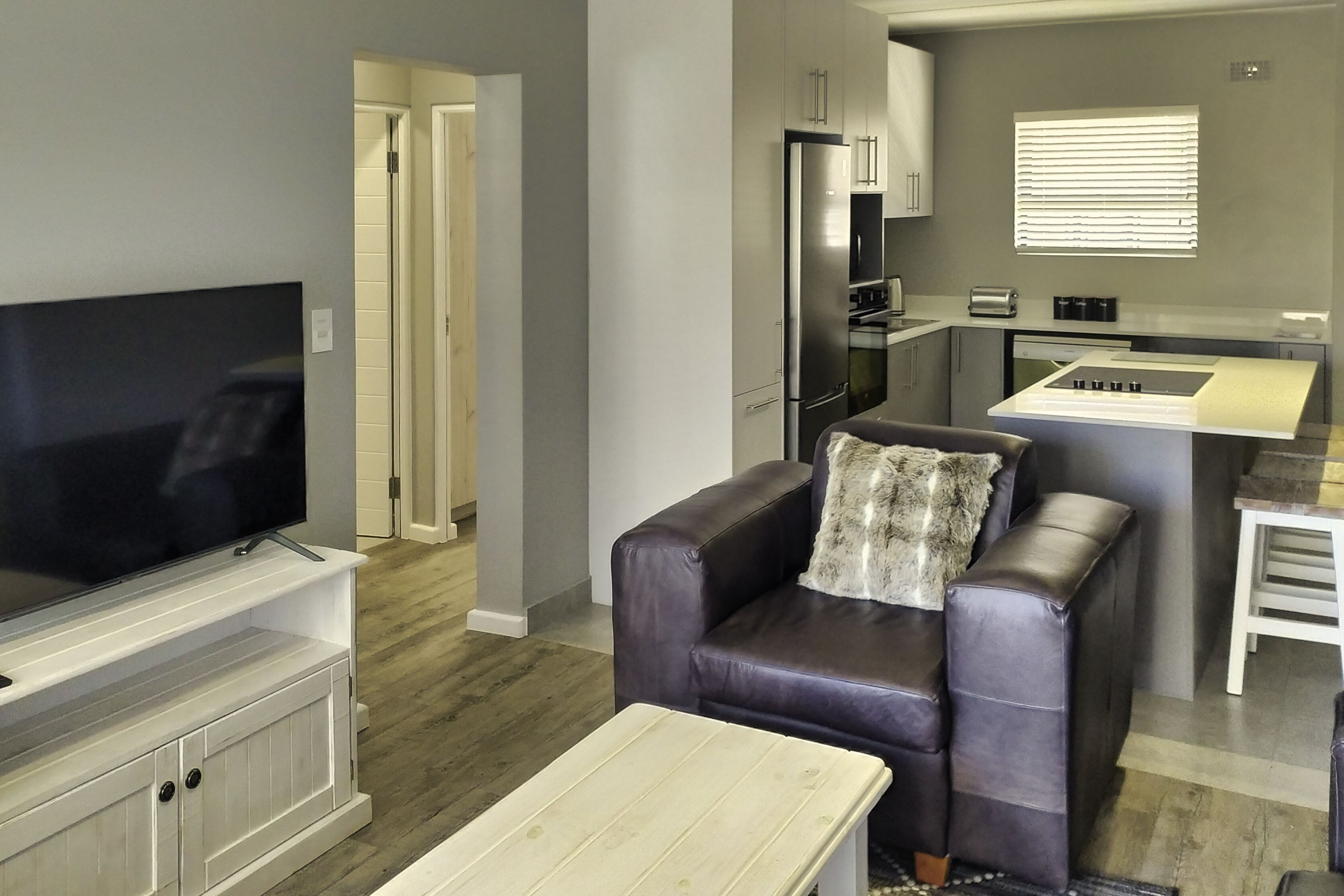 Ein modernes Wohnzimmer mit Flachbildfernseher, einer Ledersofa, einem Couchtisch und einer Küchenzeile inklusive Kühlschrank, Backofen und Spüle.