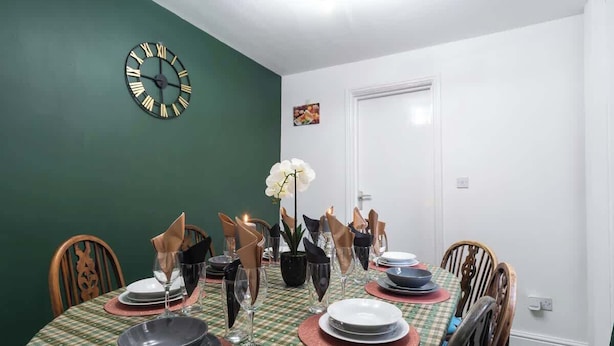 Ein Esszimmer mit grüner Wand, einer Uhr und einem Tisch für vier Personen.