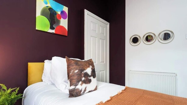 Ein Schlafzimmer mit einem Bett, einer weißen Tür, einem Heizkörper und einem farbenfrohen abstrakten Gemälde an der Wand.