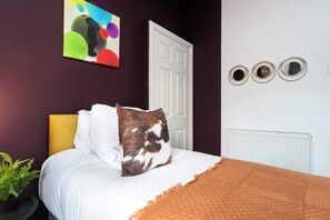 Un dormitorio con cama, una puerta blanca, un radiador y un cuadro abstracto colorido en la pared.