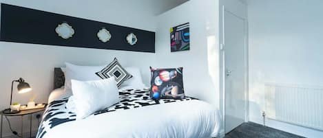 A bedroom with a bed, a nightstand, a lamp, and wall decorations.