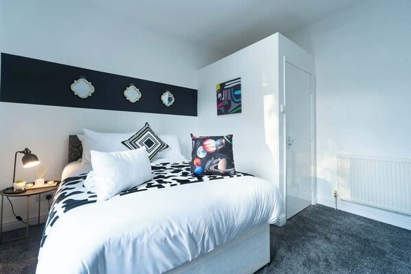 A bedroom with a bed, a nightstand, a lamp, and wall decorations.