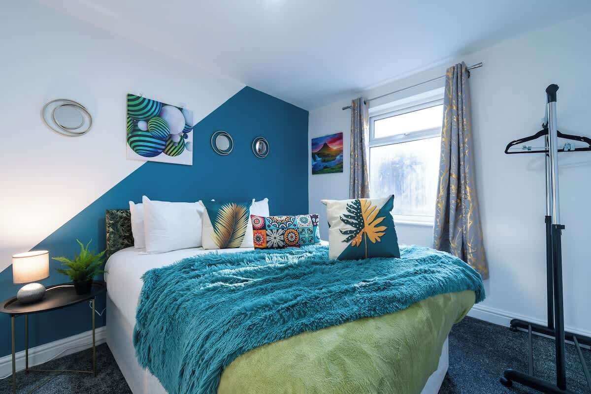 A bedroom with a bed, pillows, a nightstand, a window, and a curtain.