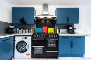 A kitchen with blue cabinets, a washing machine, a stove, and a microwave. - Homey 5 Bedrooms 9 Beds-Contractors - Leisure-Hull (Kingston upon Hull)