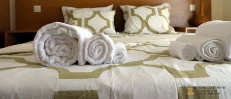 Una cama bien hecha con toallas enrolladas y almohadas estampadas, un cabecero de madera y una pared con cuadros.