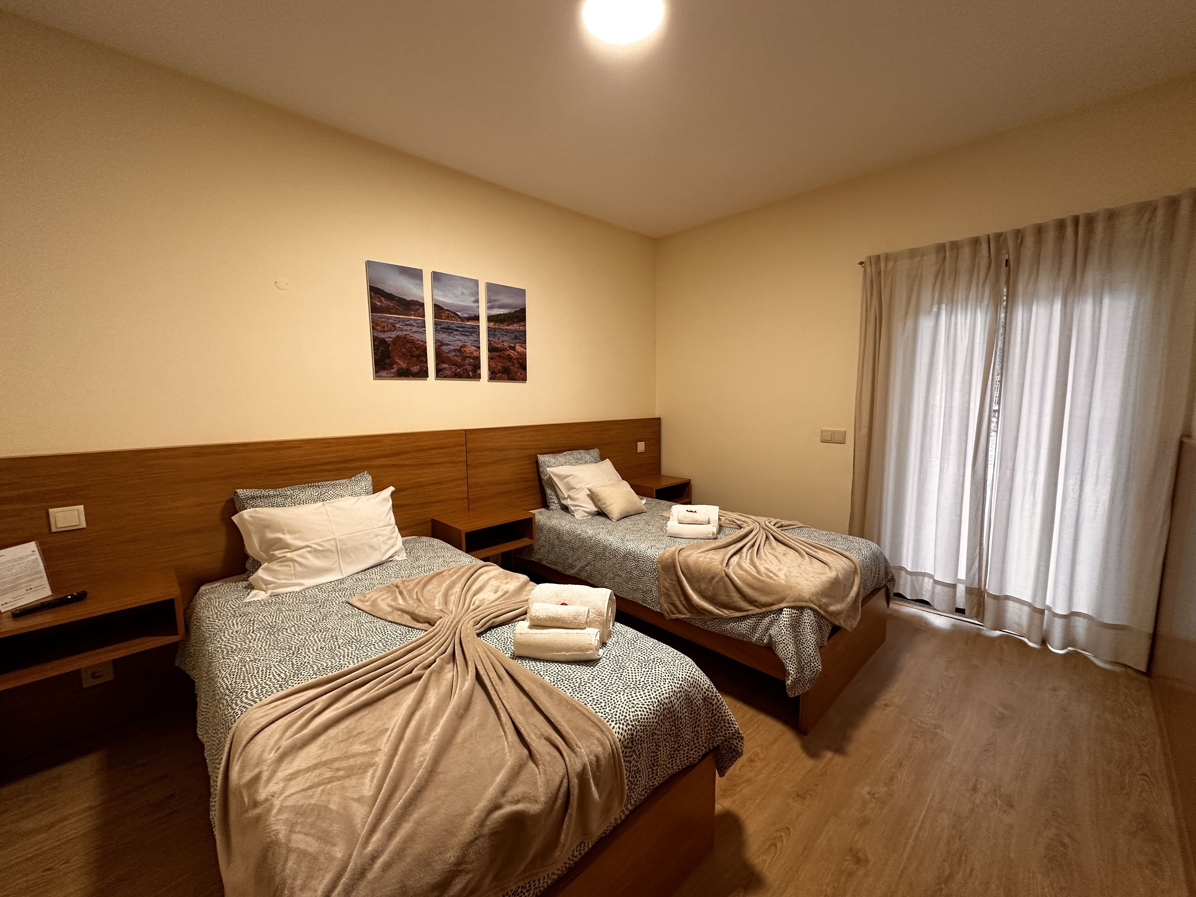 A hotel room with two beds, wooden headboards, and a large window with curtains.