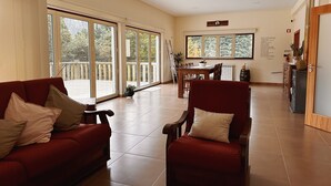 Un vaste espace de vie comprenant un canapé rouge, un fauteuil rouge et une table à manger. De grandes fenêtres offrent une vue sur l’extérieur.