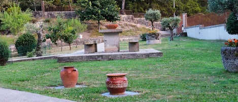 A garden with a stone bench, a large terracotta pot, and a smaller terracotta pot on the grass.