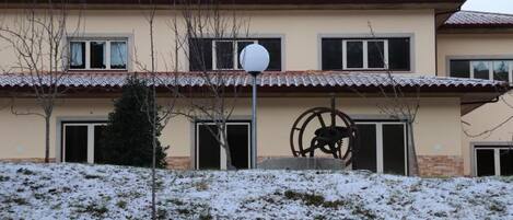 A two-story building with a red-tiled roof, a large metal sculpture in front, and a snow-covered ground.