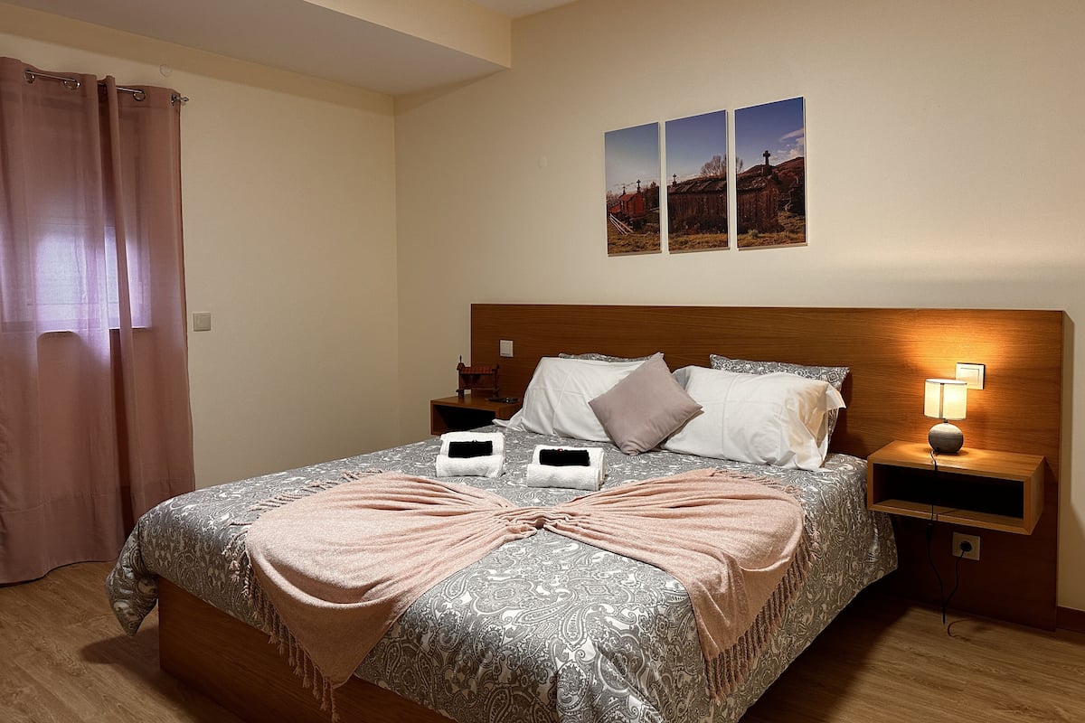 A neatly made bed with a patterned bedspread, two pillows, a bedside lamp, and a small wooden nightstand.