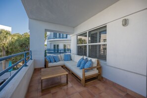 A balcony with a wooden table and a white sofa with blue patterned cushions.
