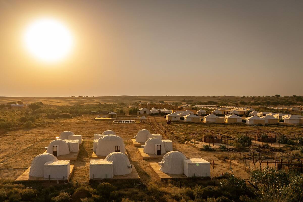 Woestijnlandschap met meerdere witte, koepelvormige tenten die in rijen staan, wat wijst op een tijdelijke verblijfsopstelling.