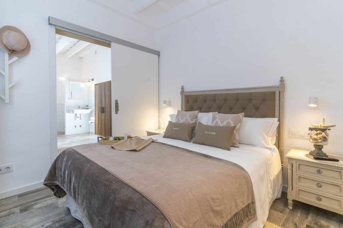 A bedroom with a large bed, a nightstand with a lamp, and a view into the bathroom.