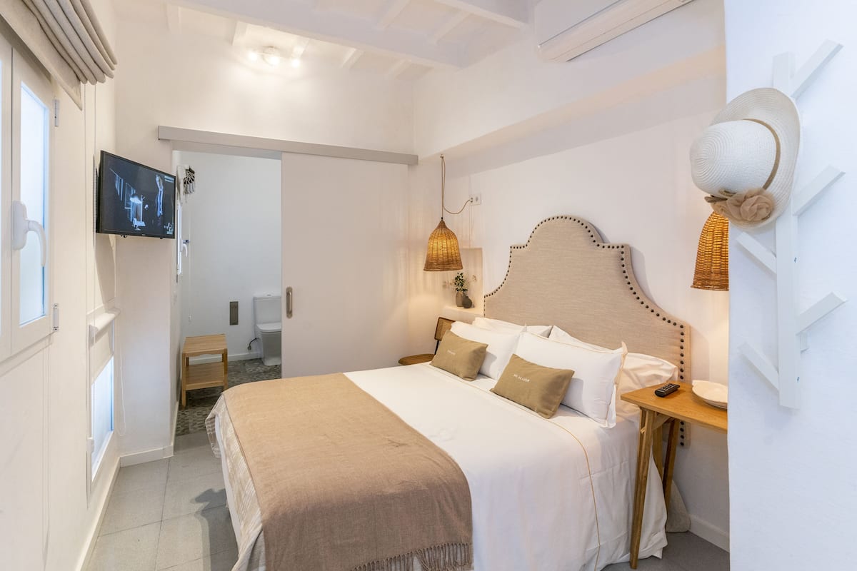 A bedroom with a bed, bedside table, lamp, and a television on the wall.