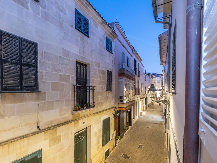 A narrow street with buildings on either side, featuring stone facades and shutters.