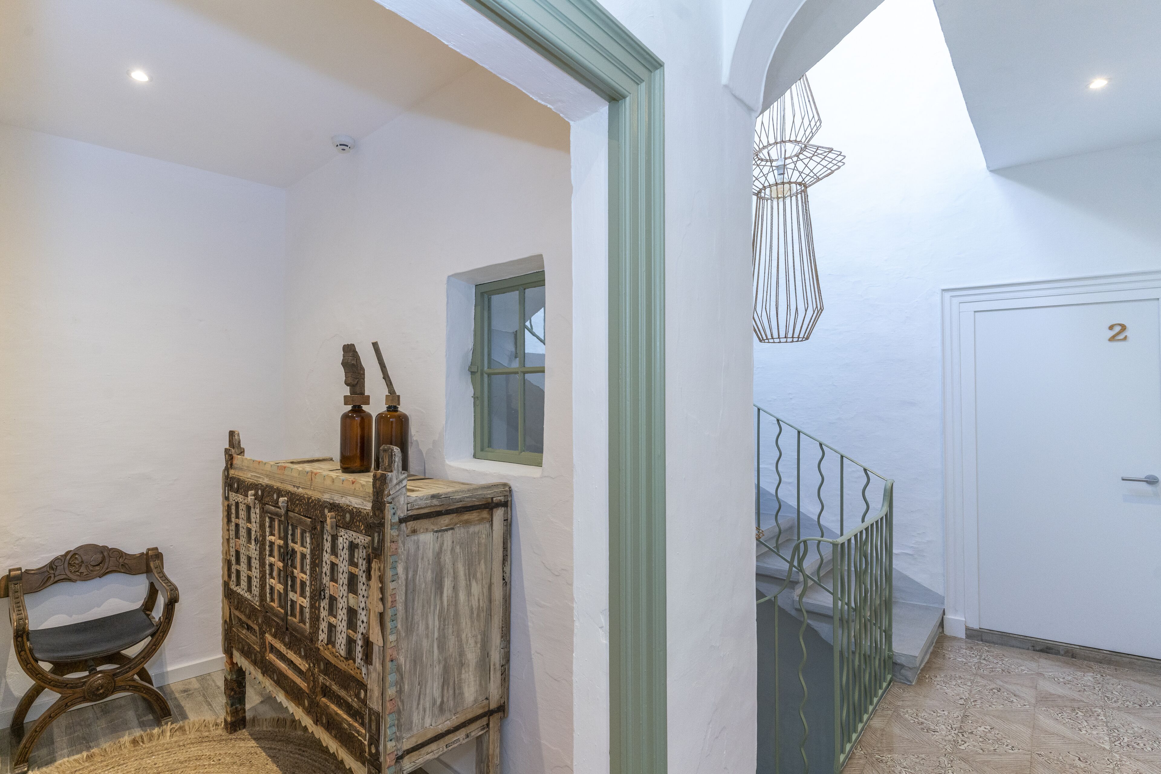 Un pasillo con un banco de madera, un aparador rústico, un ventanal pequeño y una puerta con el número 2.