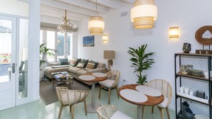 A modern living room with a sofa, coffee table, and chairs, a dining area with a table and chairs, and a bookshelf. - Encant de Alaior Boutique Hotel  (Alayor)