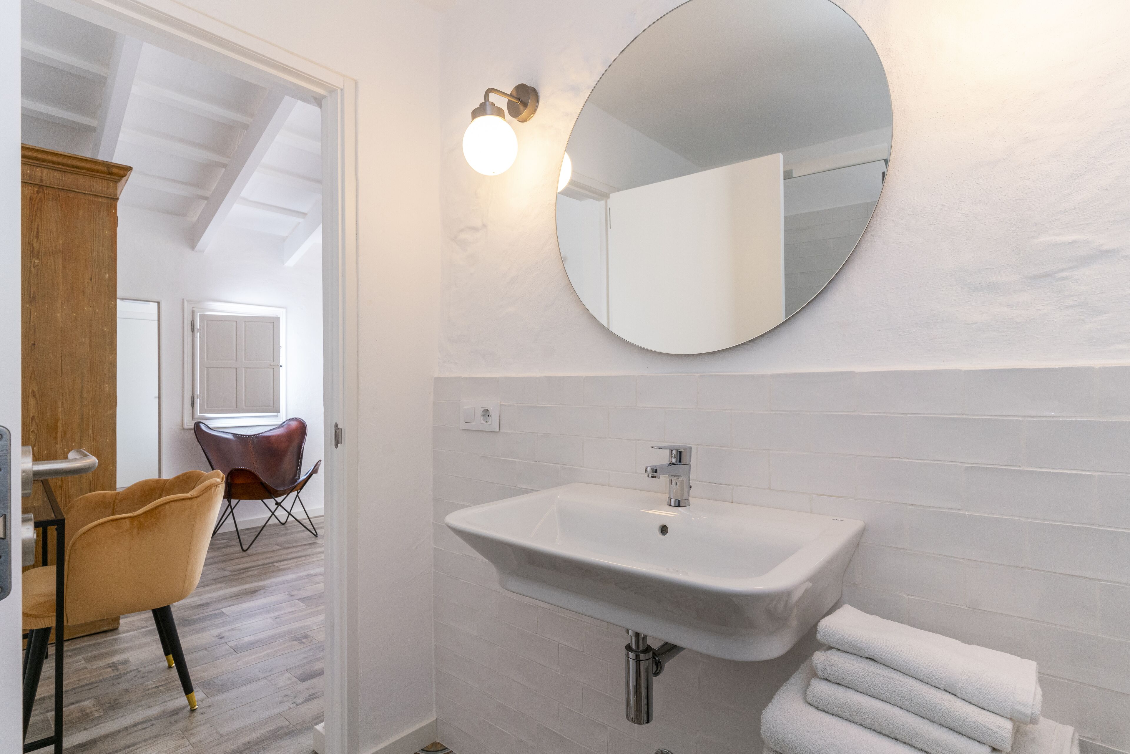 A bathroom with a white sink, a round mirror, and a wooden cabinet.