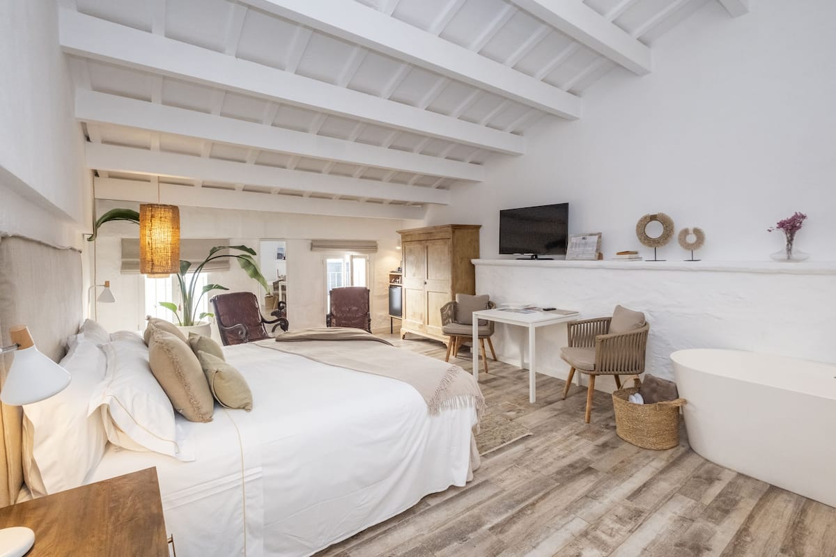 A spacious bedroom with a large bed, a desk, a chair, a television, and a bathroom.