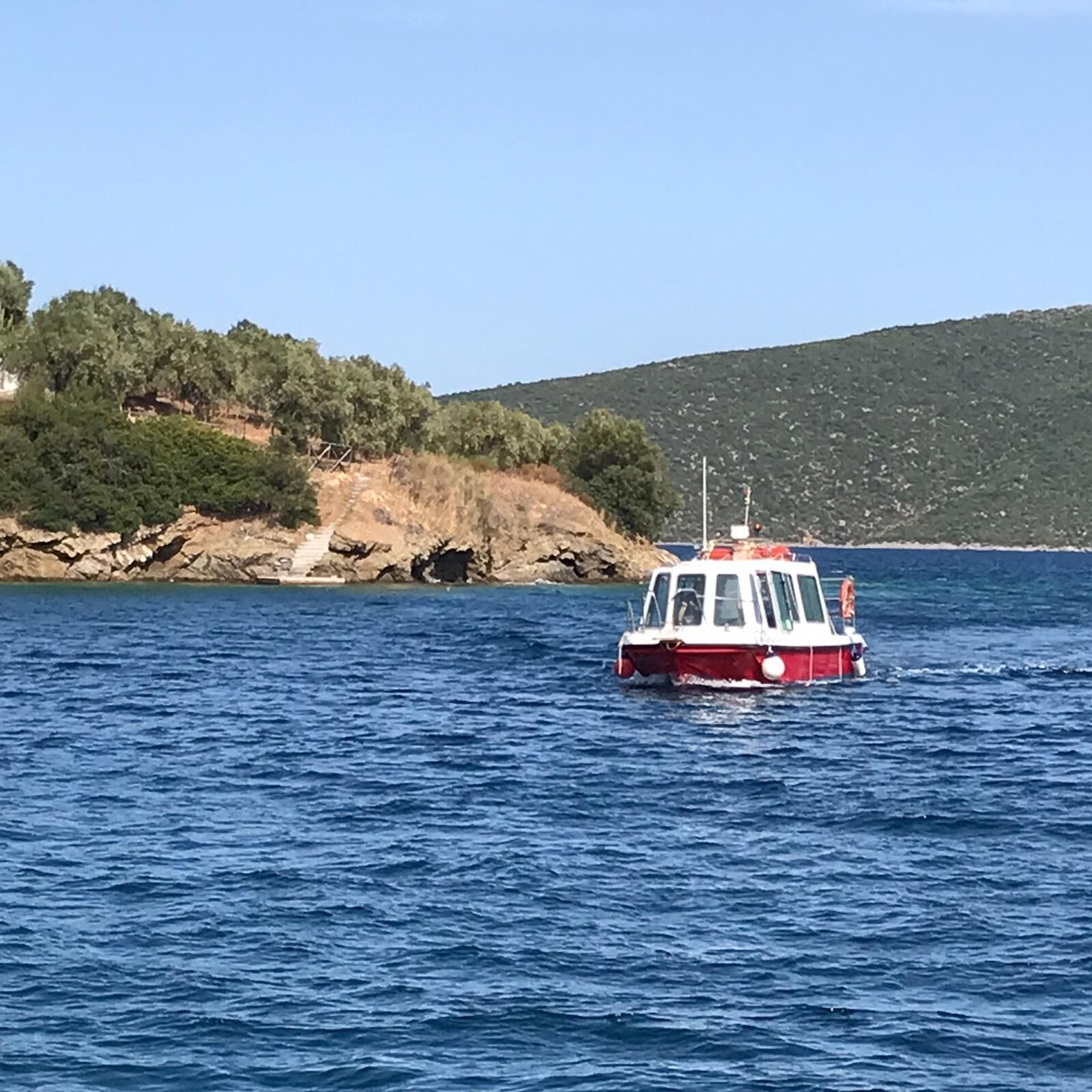 A boat on a body of water with a rocky coastline and greenery in the background.