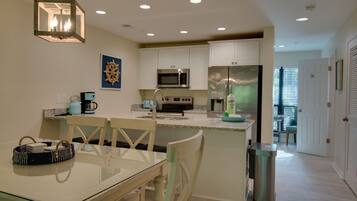A modern kitchen with white cabinets, stainless steel appliances, and a glass dining table.