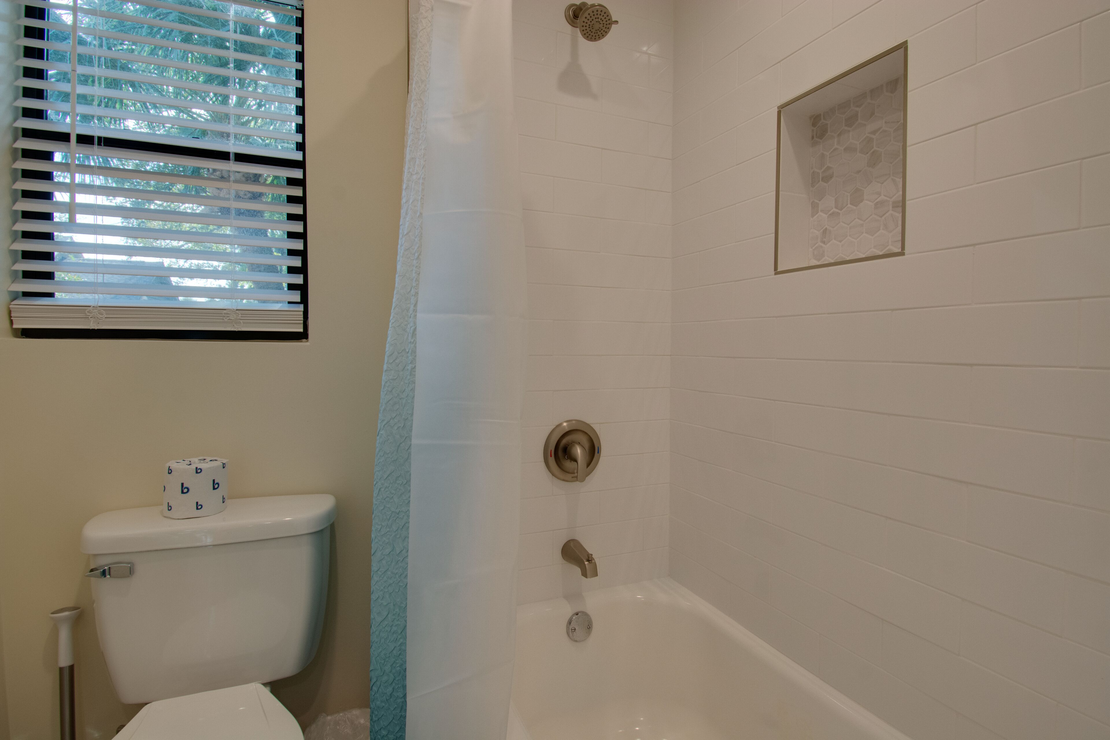 Ein Badezimmer mit Toilette, einer Dusche mit Glastrennwand und einem Fenster mit Jalousien.